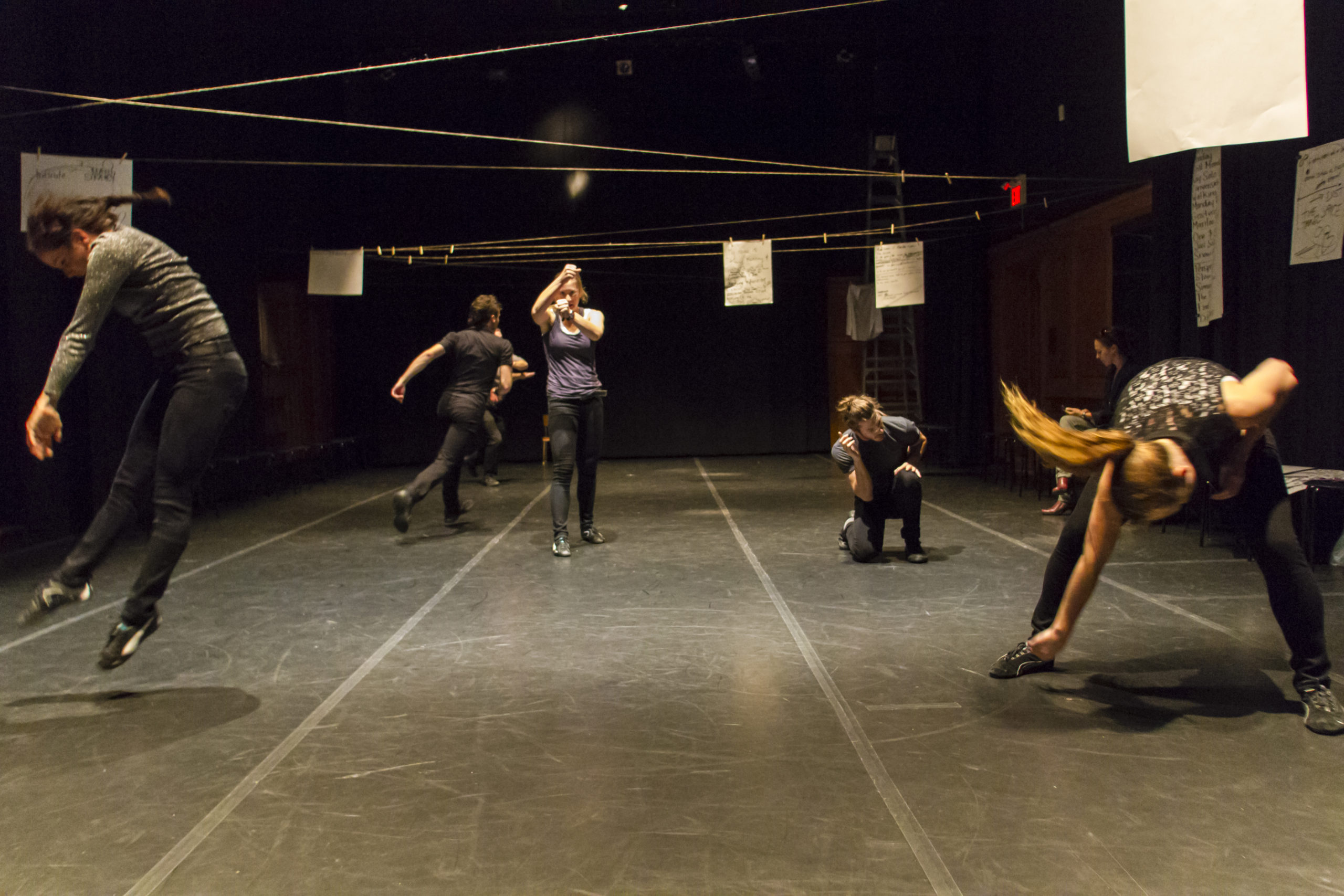 Five contemporary dancers move in different ways on a set. / Cinq danseurs contemporains dansent sur une scène.