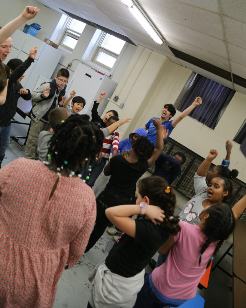 A cluster of children cheer, raising one fist in the air. / Un groupe d’enfants crient de bonheur, levant un poing au ciel.