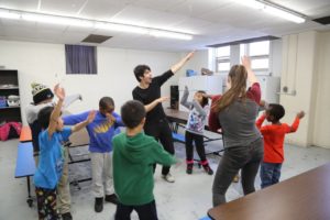 A man teaches children a dance move. / Un homme enseigne un pas de danse à des enfants.