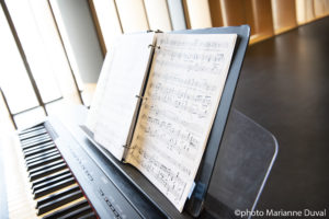 An open binder of sheet music above an electric piano. / Un classeur ouvert rempli de partitions au dessus d'un piano électrique.