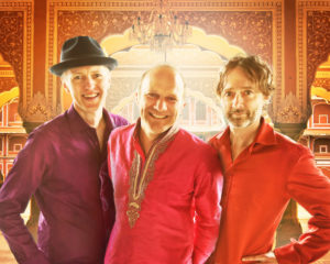 Three White men smile at the camera in front of a backdrop. / Trois hommes Blancs sourient à la caméra devant une toile de fond.