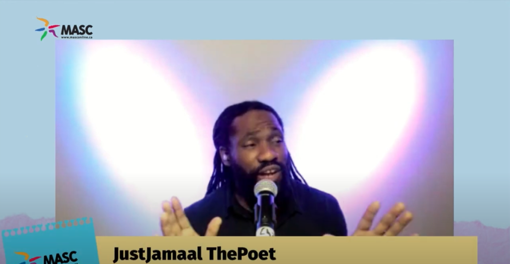 JustJamaal thePoet in front of a microphone with is hands up and eyebrows raising while. He is explaining something and his hair is tied up halfway with some strands in the back.