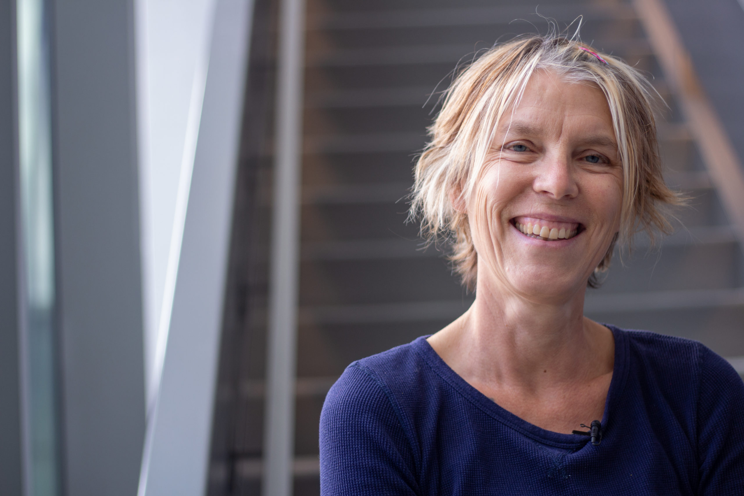 A smiling White woman with short blonde hair and blue eyes. / Une femme Blanche souriante aux cheveux blonds et courts et aux yeux bleus.