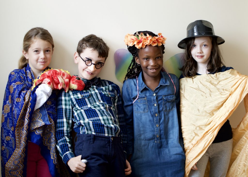 Four children in costumes smile. / Quatre enfants costumés sourient.