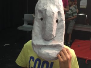A child wears a large white mask. / Un enfant porte un grand masque blanc.