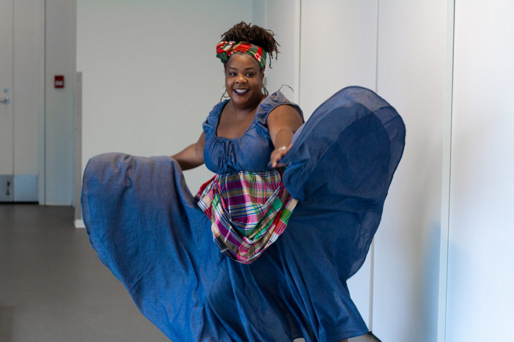 A Black woman smiles while she twirls her blue dress. / Une femme Noire sourit et fait virevolter sa robe bleue.