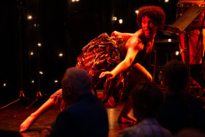 Julianne dancing, wearing colourful patterned fabric under warm stage lighting.